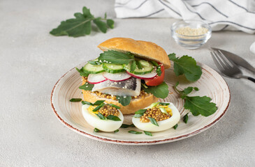Homemade sandwich with salted herring, cucumber, tomato, arugula and radish served of boiled egg and mustard on gray plate, Close up