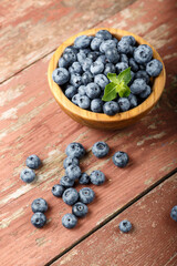 Blueberry berries with mint leaves are in a wooden plate on wooden background.