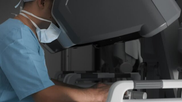 Unrecognizable doctor performs surgery using medical robot in advanced operating room. Surgeon controls robotic arms with manipulator and virtual reality headset