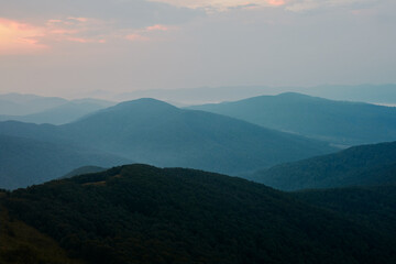 Sunset in mountains. Natural mountain landscape with illuminated misty peaks, foggy slopes and valleys, blue sky with orange yellow sunlight