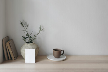 Moody wedding stationery. Vertical blank greeting card, invitation. Old vase with olive branches and books on wooden table. Summer Mediterranean design. Elegant working space, home office. No people.