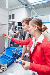 Worker and manager on factory floor discussing product specifications looking at a plan sheet