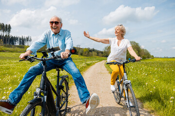 Seniors having fun on bicycles in spring landscape - 602591470