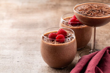 Homemade chocolate mousse decorated with raspberries and dark chocolate sprinkles in portion glasses. Brown table. Selective focus, copy space.
