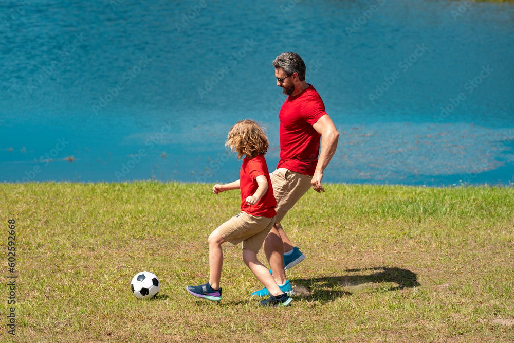 Sticker Dad and son playing football together on green meadow. Father and son having fun on football pitch. Dad with kid are having fun and playing football on grass outdoor. Friendly family. Fathers day.