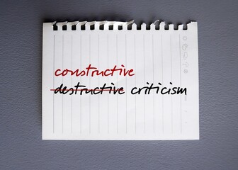 Torn paper on gray background with handwritten text DESTRUCTIVE CRITICISM, changed to CONSTRUCTIVE...