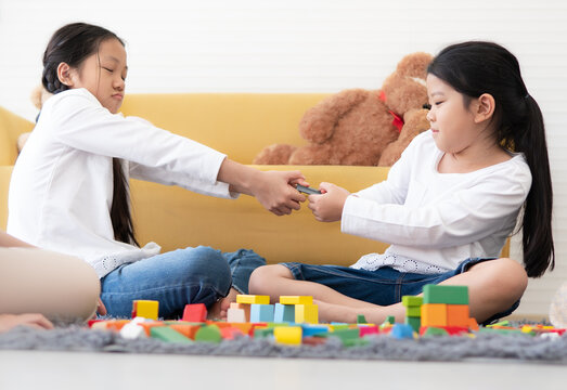 Naughty girl play block game and snatch toy from her sister. Asian kids have fun family leisure activity together playing and funny fighting at home. Female child pulling snatching with her sibling.