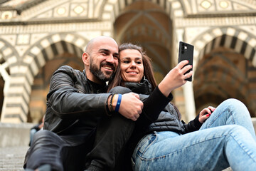  Happy smiling beautiful  Tourists  couple traveling in Italy poses and making photos near the Cathedral of Amalfi  .Family on vacation on Amalfi coast in Italy. 