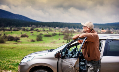 Young adult male traveler standing next to the car and admiring the mountain landscape