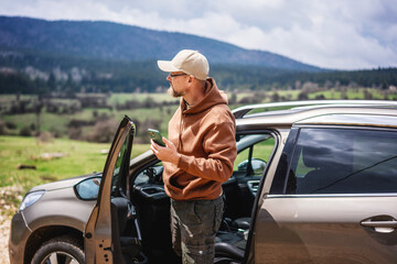 Naklejka premium Man travel by car and using smartphone in mountains on vacation trip, making browsing phone and gps.
