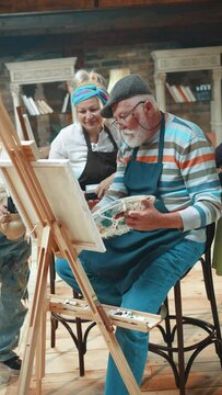 Vertical shot of a old retired couple paints with acrylic paints on a canvas having an art class with a teacher and friends