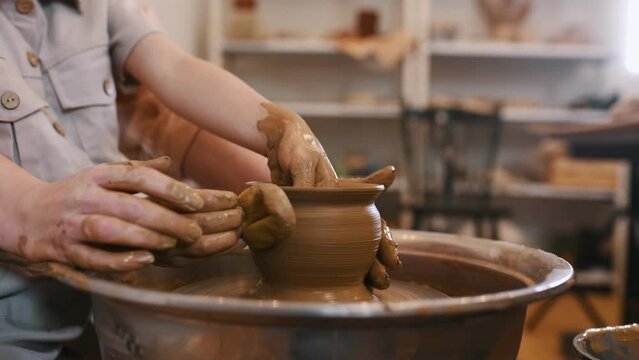 Focuced close up view. Using the pottery wheel to shape the clay. Mother is with little girl.