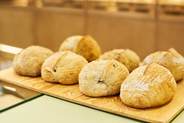 Several loaves of fresh wheat bread on wooden board or tray on display or counter desk prepared for selling to customers of bakery shop