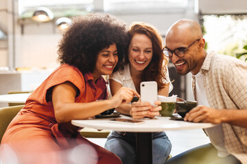 Three happy friends browsing social media on a smartphone during their coffee break