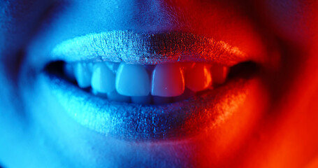 Close up shot of lips of a young girl with glowing makeup making a beautiful positive sensual smile in neon light - emotions, nightlife concept 