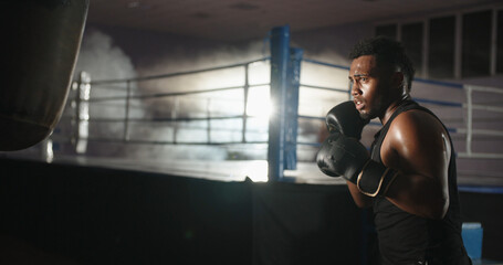 African american athlete is training in a gym, hitting a punching bag in boxing gloves, keeping fit...