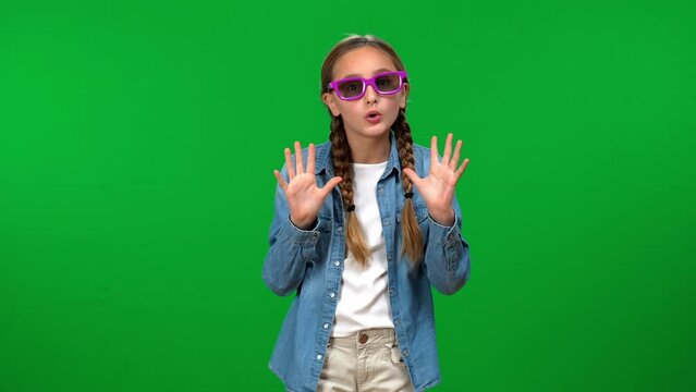 Excited teen girl putting on violet 3D glasses smiling gesturing at green screen background. Portrait of joyful happy Caucasian teenager watching movie on chroma key