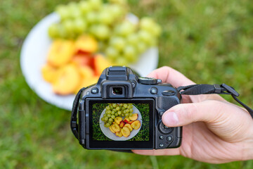 Talerz z owocami nektarynkami j winogronem na ekranie aparatu fotograficznego trzymanego w dłoni 