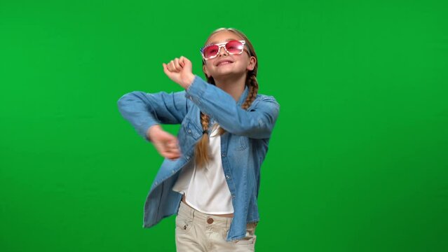Happy teen Caucasian girl in sunglasses dancing at chroma key background smiling. Portrait of excited cheerful teenager having fun enjoying leisure on green screen