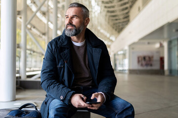 a mature adult male financier with gray hair and a beard with a phone in his hands sits in the...