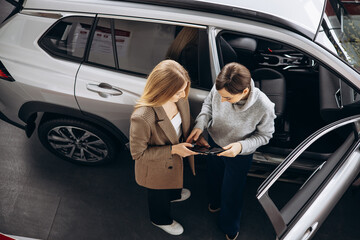 Woman choosing a car with dealership in a car showroom