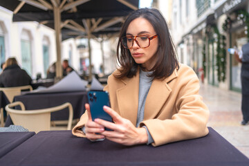 Middle-aged woman using smartphone sitting outdoor cafe