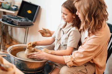 Sitting, creating the shape. Mother with little girl doing pottery at home