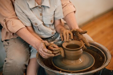 Using clay to create the pot. Mother with little girl learning pottery in the workshop