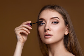 young woman applying black mascara on long thick eyelashes