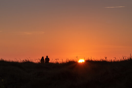 couple sitting in a meadow watching the sunset against an orange sky