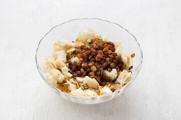 Glass bowl with pieces of puff pastry, nuts and raisins for a delicious arabic umm ali dessert or other dish on a light gray background. Cooking stage - 602615205