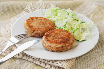 Fish cakes, or cutlets. Made from ground perch and tuna with herbs, breaded and fried, served with salad on a white plate