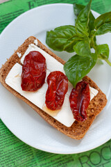 Bruschetta with olive oil, sundried tomatoes, feta and fresh basil on a white plate, green napkin, wooden table