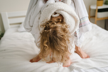 Mom puts a towel on girl kid head. Young mother with cute little daughter in bathrobe towel on heads standing on bed lovely. Healthcare and family concept. Cheerful beauty day at home. Closeup.