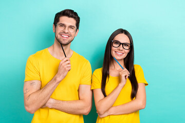 Photo of two minded optimistic cheerful wear yellow t-shirt hold pencil writers youngsters man with girlfriend hold isolated cyan color background