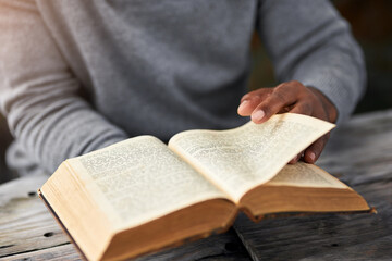 Hands, book and a man reading the bible at a table outdoor for faith or belief in god closeup. Religion, story and spiritual with a male christian sitting down to read for learning or worship