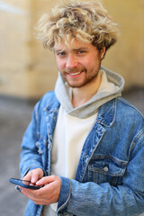 Curly young guy with a beard holds smartphones in his hands smiling.