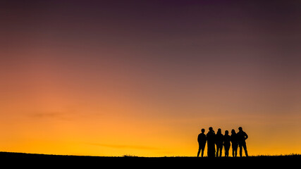 Naklejka na ściany i meble A silhouette of a group of people at sunset in Monjong, Chiangmai, Thailand. Group People relaxing and Standing Silhouette Concept. Silhouette of group happy traveler team on high land and sunset time