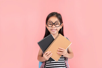 schoolgirl hugging book wearing backpack smiling isolated on pink background