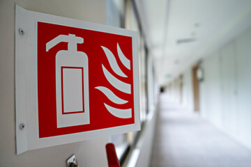 Close-up image features an emergency sign of a fire extinguisher in a building corridor. The image...