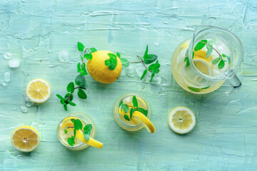 Lemonade with mint. Lemon water drink with ice. Two glasses and a pitcher on a blue background,...