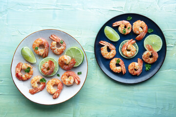 Shrimps, top flat lay shot on a teal blue background. Cooked shrimp with lime, spicy seafood dish