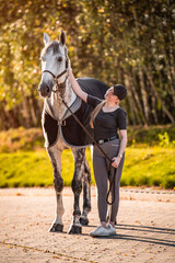 Female equestrian horse rider patting her gray horse.