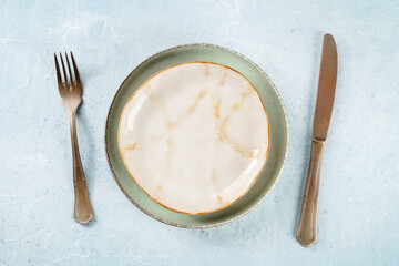 An empty plate with a gold rim, with silverware, overhead flat lay shot. Modern tableware