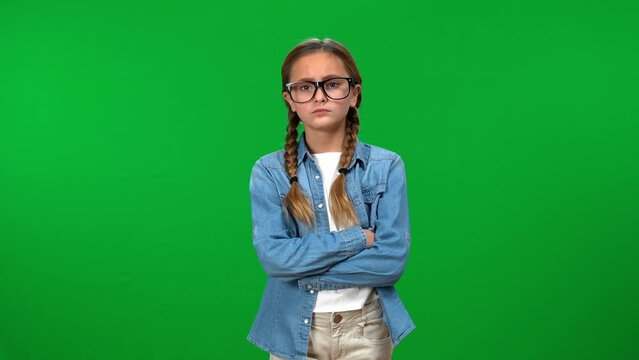 Intelligent dissatisfied nerd teen girl in eyeglasses crossing hands looking at camera on green screen. Front view portrait of Caucasian smart teenager posing with unsatisfied facial expression