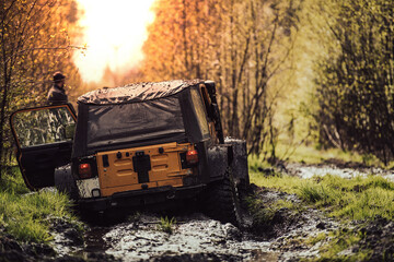 Fototapeta na wymiar Offroad vehicle driving through the mud towards the setting sun.