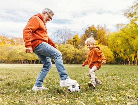 Happy family grandfather and grandson play football on lawn in park.