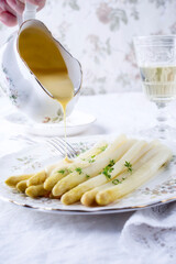 Classic style traditional white asparagus served with sauce holhollandaiseandaise from a sauce boat in hands on a man as close-up on a design plate