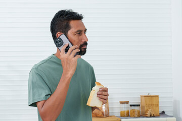 Bearded Asian man wearing comfortable pajamas clothes on holiday morning, waking up phone call from...