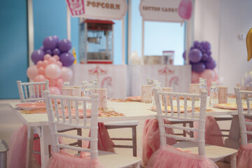 Kids little girls birthday party. A white table and chairs with pink and purple decorations and...